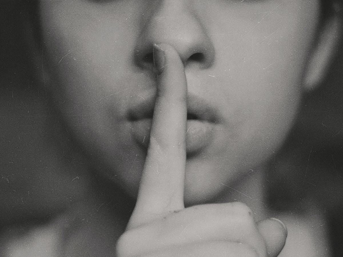 Woman gesturing "shh" with her pointer finger over her lips.